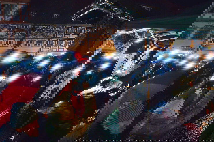 Eine Menschenmenge steht abends mit Lichtern vor einer Bühne.