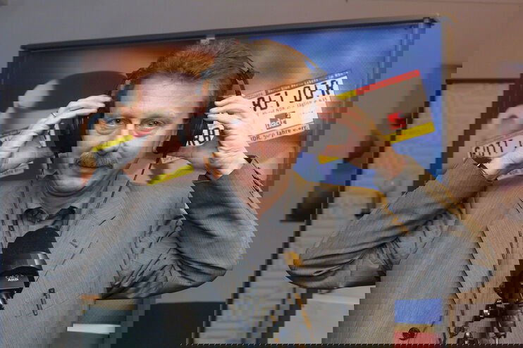 Ein Mann mit Schnurrbart mit Kopfhörer vor einem Mikrofon.