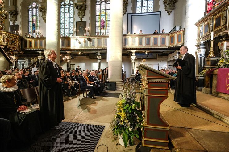 Zwei männlich zu lesende Personen im Taler stehen sich im Altarraum einer Kirche gegenüber.