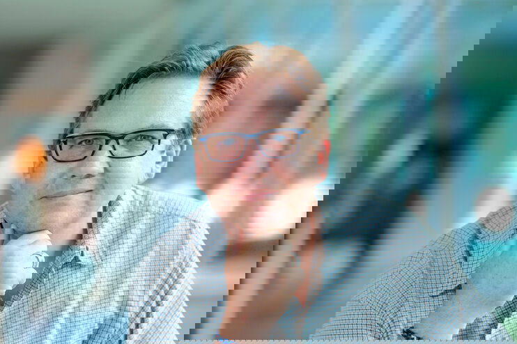 Ein Mann mit Brille und kariertem Hemd stützt seinen Kopf nachdenklich auf die Hand.