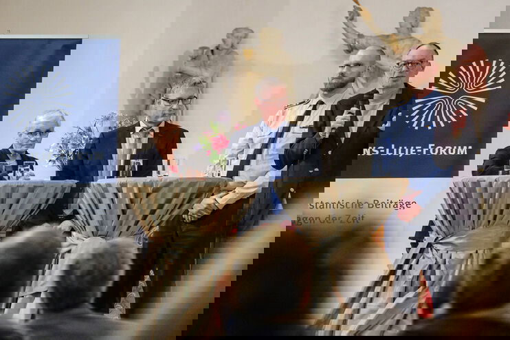 Eine Frau und drei Männer (einer davon in Uniform) stehen an Stehtischen und diskutieren.