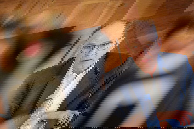 Ein Mann mit hoher Stirn und Brille sitzt vor einem Mikrofon.