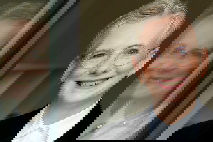 eine Frau lehnt sich an einer Glastür an. Links spiegelt sich ihr Kopf in der Tür.