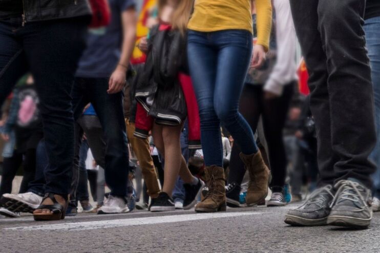 Blick aus der Froschperspektive auf eine Straße, auf der viele Menschen laufen, man sieht nur Schuhe und Beine.