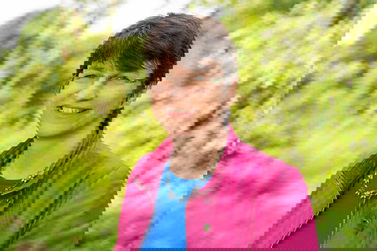 Eine als Frau lesbare Person steht im Grünen.