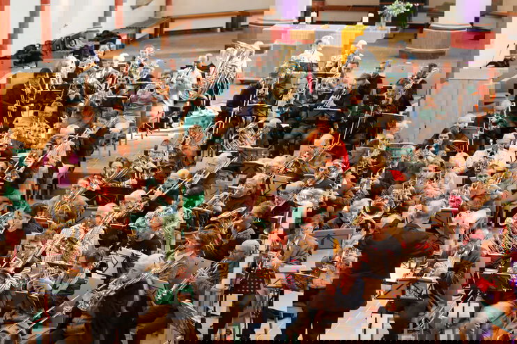 Viele Menschen sitzen in einem Raum und spielen verschiedene Blasinstrumente.