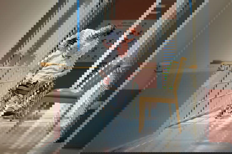 Eine Pflegerin mit Mundschutz schiebt einen Mann im Rollstuhl.