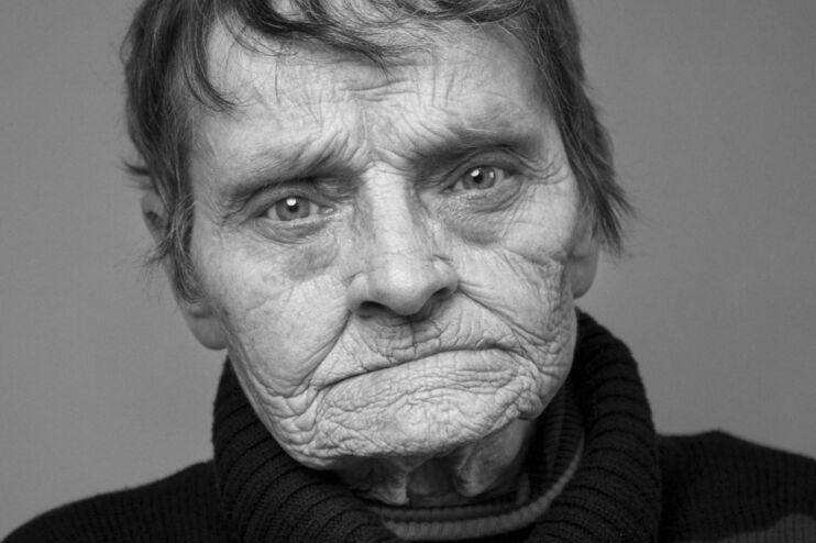Eine Schwarzweißfotografie von einer als Frau lesbaren Person mit kurzen Haaren und faltiger Haut.