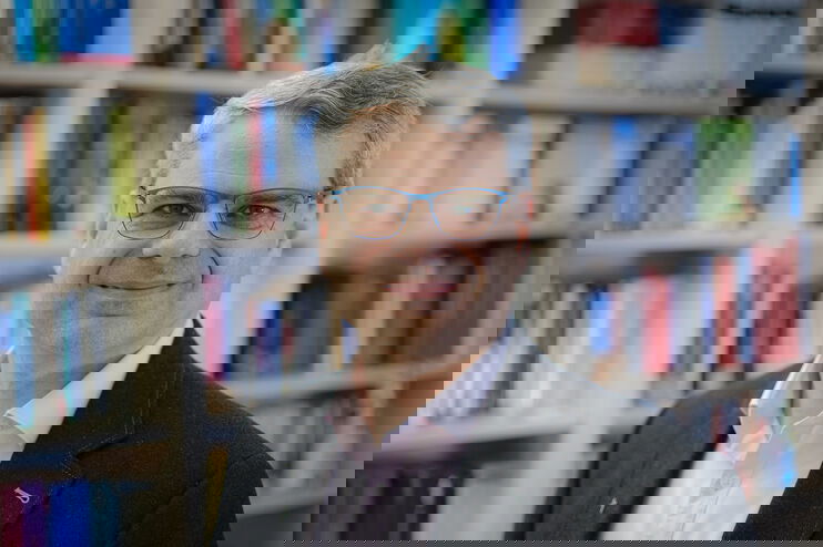 Eine als Mann lesbare Person vor einer Bücherwand.