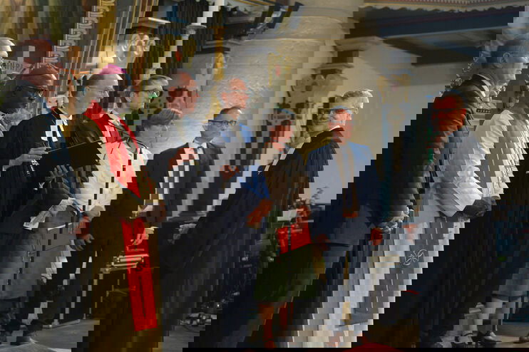 Mehrere Männer stehen in einer Kirche in einer Reihe. Vor ihnen steht ein Mann, der in die Kamera blickt.