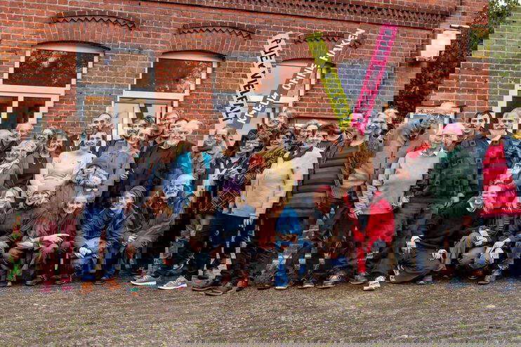 Eine Gruppe von Menschen steht vor einem Backsteinhaus.