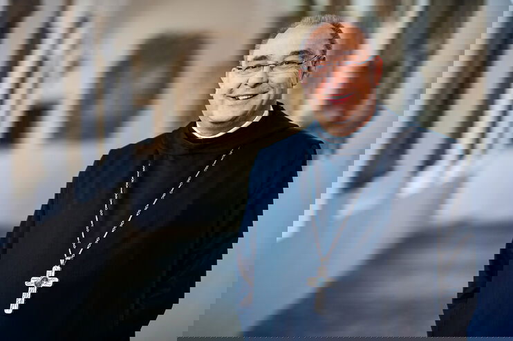 Eine als Mann lesbare Person steht im Bischofsornat in einem historischen Gang.