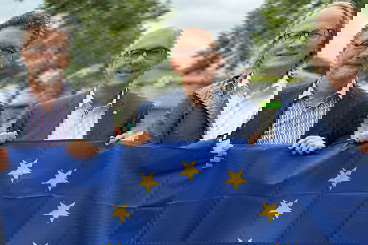 drei männlich gelesene Personen halten eine Europaflagge in der Hand.