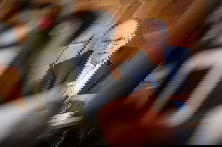 Eine als Mann lesbare Person spricht mit nachdenklichem Gesicht in Fernsehkameras.