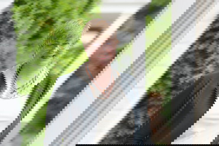 Eine als Frau lesbare Person steht im Freien zwischen weißen Säulen.