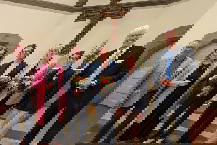 Eine Gruppe aus weiblich und männlich lesbaren Personen steht vor einem Altar in einer Kirche.