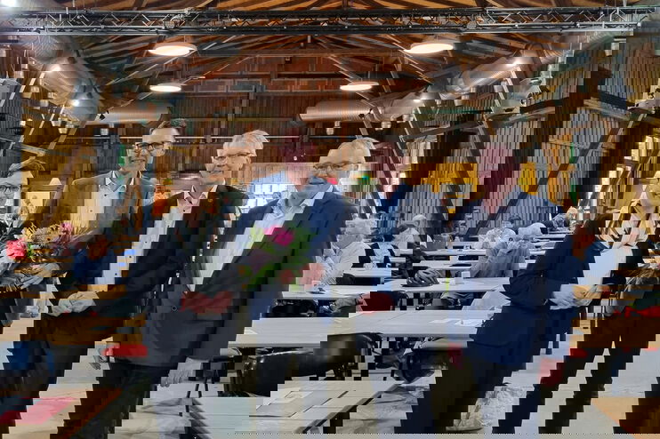 Eine als Frau lesbare Person und drei als Männer lesbare Personen stehen in einem Saal.