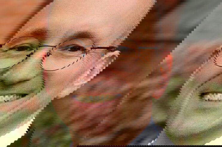 Eine als Mann lesbare Person mit hoher Stirn und Brille.