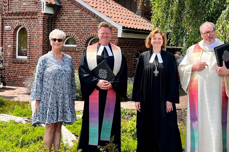 eine Gruppe von Menschen vor einer Autobahnkirche aus Backstein an einem Sommertag