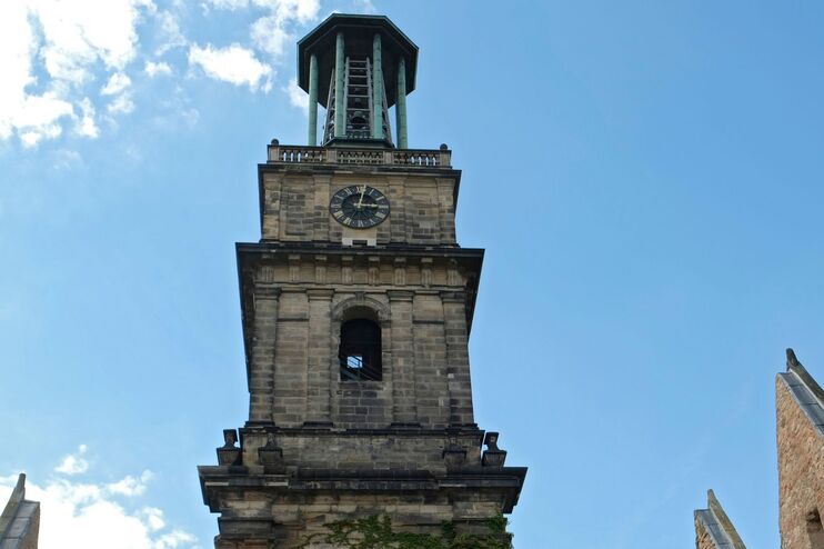 Ein Kirchturm mit einer Uhr vor blauem Himmel.
