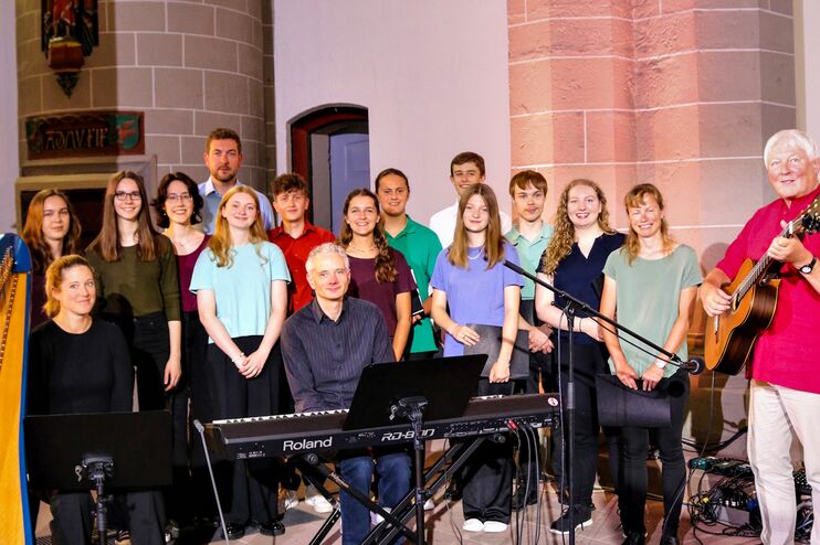 Mehrere Menschen stehen neben einer Harfe. Eine männlich gelesene Person steht rechts mit einer Gitarre.