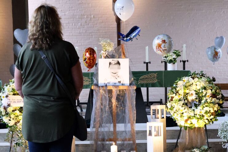 Blumen und Kerzen in einem Kirchenaltar. In der Mitte eine Zeichnung von einem Kind. Links steht eine junge Frau und schaut auf die Zeichnung.