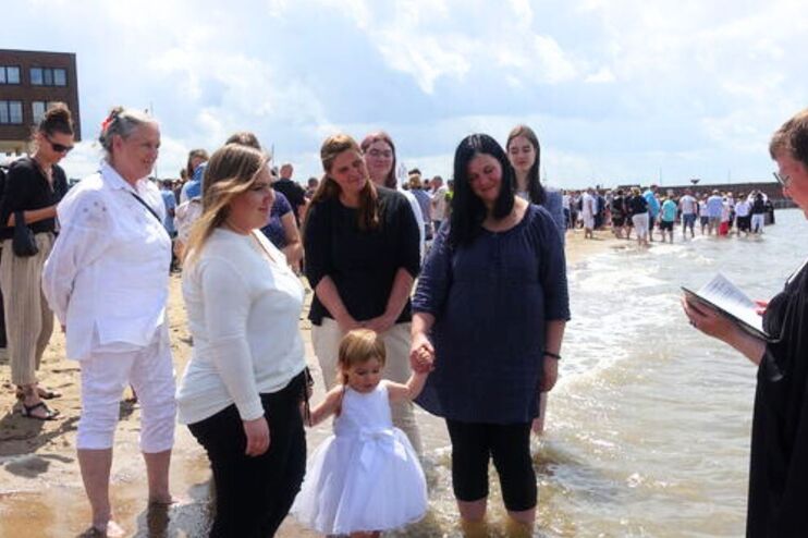 Menschen mit einer Pastorin an einem Flussstrand.