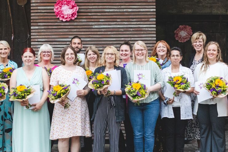 eine Gruppe von Menschen mit Blumensträußen in der Hand vor einem Gebäude