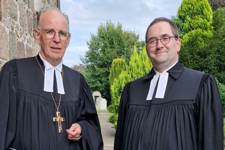zwei Männer in Talaren vor einer Kirche