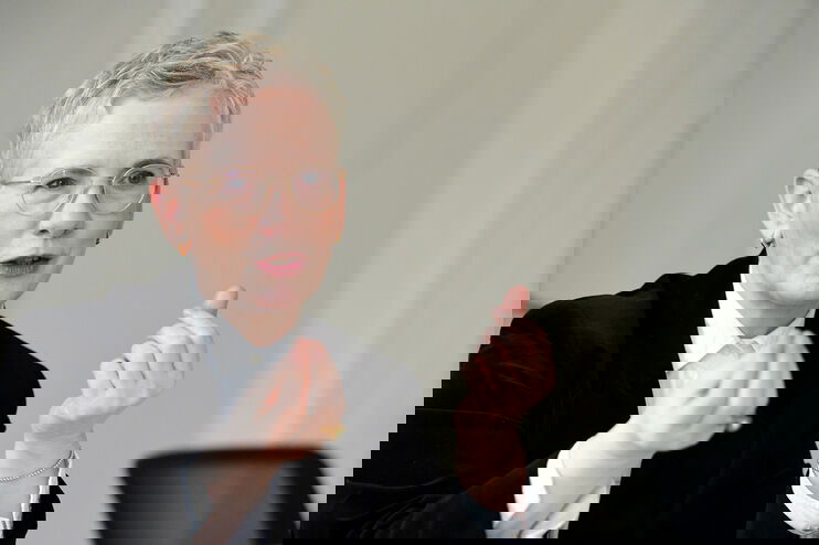 Eine als Frau lesbare Person mit kurzen blonden Haaren spricht und gestikuliert dabei.