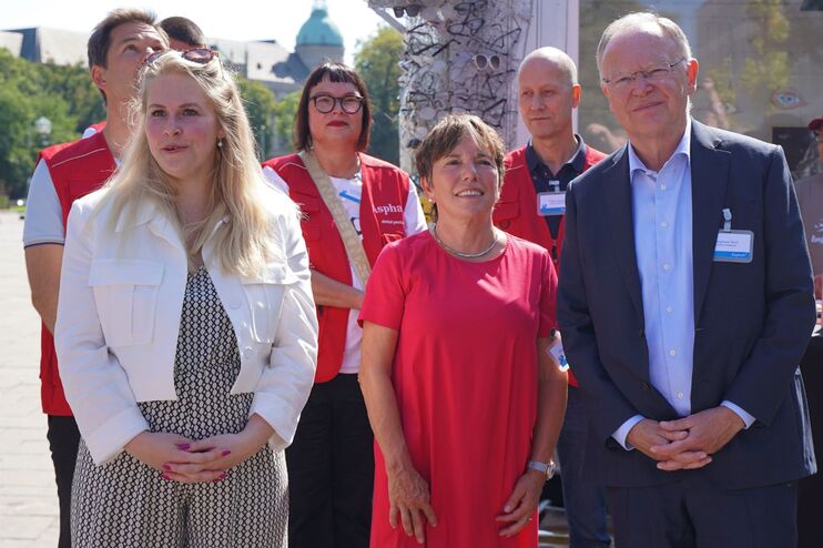 eine Gruppe von Menschen  vor einem Gebäude. Links ein Plakat. Darauf ist ein Magazincover.