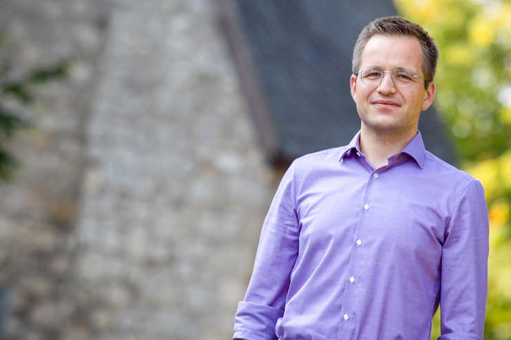 Eine männlich gelesene Person in einem lilafarbenem Hemd.