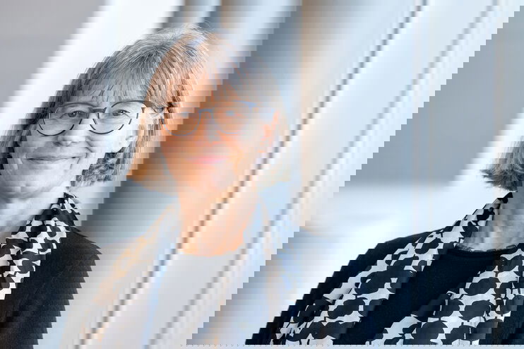 Eine als Frau lesbare Person mit halblangen grauen Haaren, Brille und gepunktetem Halstuch.