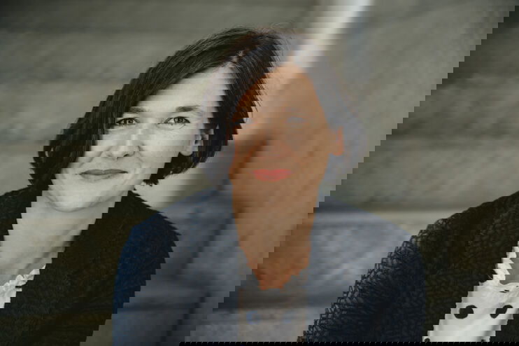 Portraitfoto einer als Frau lesbaren Personen mit schulterlangen dunklen Haaren.