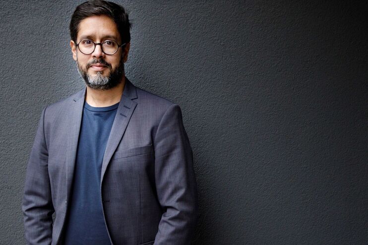 ein Mann vor einem dunklen Hintergrund schaut freundlich in die Kamera.