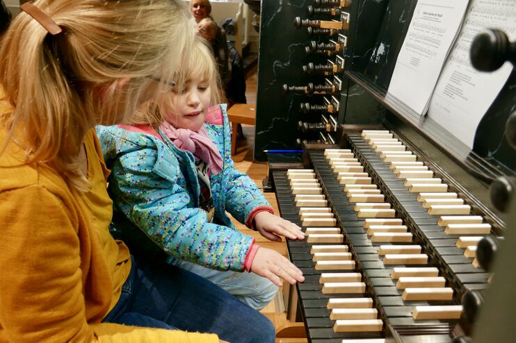 Eine erwachsene Person sitzt mit einem Kind an den Tasten einer Orgel.