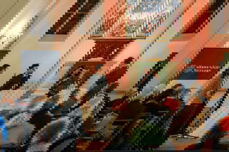 Vier Personen stehen in einem Halbkreis vor in Bänken sitzenden Menschen in einer Kirche.