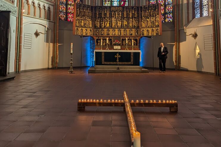 Blick in den Altarraum einer Kirche. Auf dem Boden bilden Kerzen ein Kreuz. Links und rechts des Altars sind die Wände blau beleuchtet.