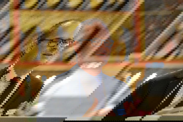 Eine als Mann lesbare Person im Anzug und mit hoher Stirn spricht in einer Kirche an einem Pult.