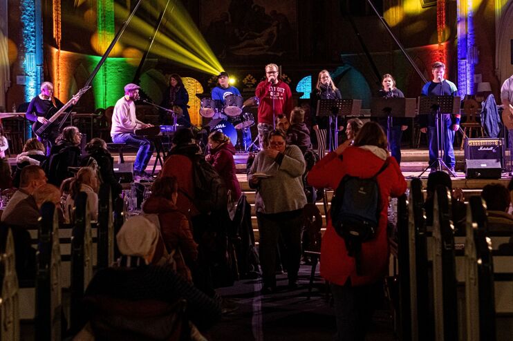 eine Band spielt in einer Kirche vor Publikum. Bunte Scheinwerfer strahlen in den Kirchraum.