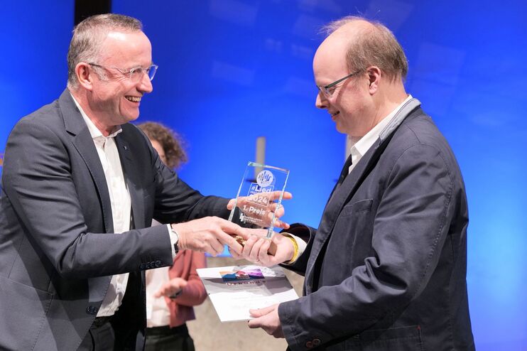 Ein Mann bekommt auf der Bühnen einen Preis überreicht.