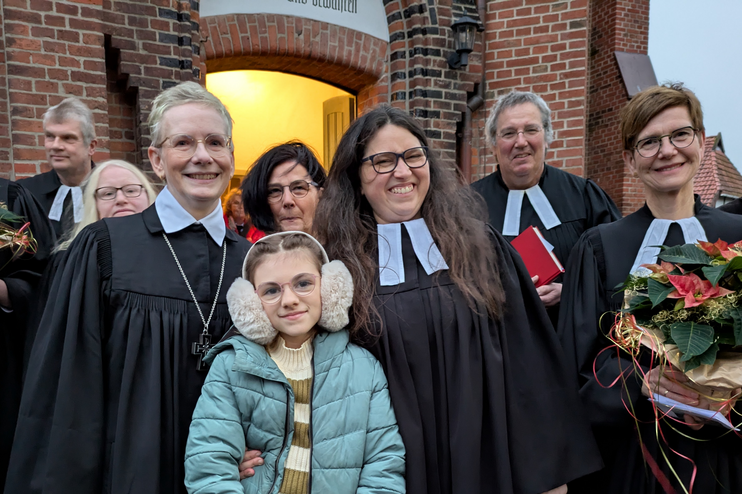 Mehrere Personen, teils in Talaren oder mit Winterjacken, stehen im Eingangsportal einer Kirche.