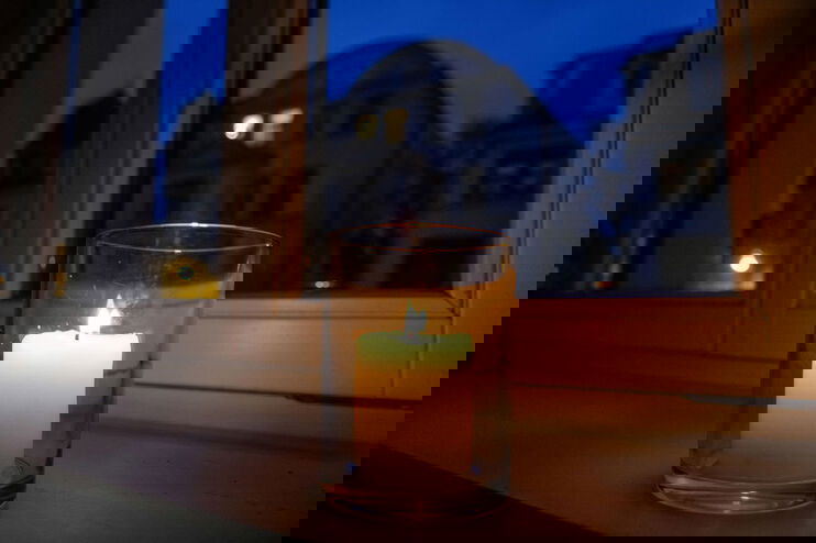 Eine Kerze brennt in einem Glas, das auf einer Fensterbank steht. Draußen ist es dunkel. 