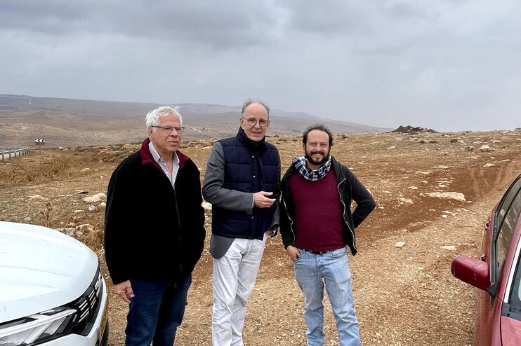Drei männlich gelesene Personen stehen vor einer Geröllbrache im Westjordanland zwischen zwei Autos.
