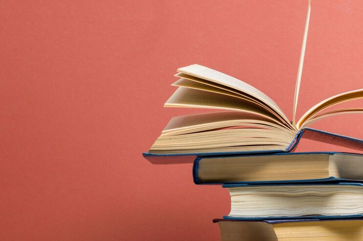 Ein Stapel Bücher, das oberste aufgeschlagen, vor einer roten Wand.