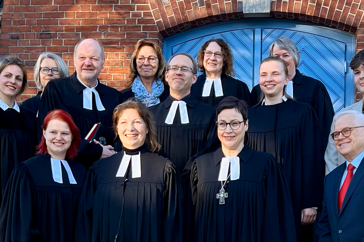 Mehrere Personen, teils in Talaren, stehen vor einer blauen Holztür in einem großen Gebäude.