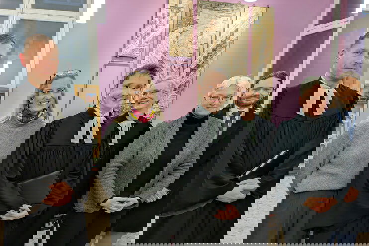 Eine Gruppe aus weiblich und männlich lesbaren Personen posieren als Gruppe, zwei davon im Talar.