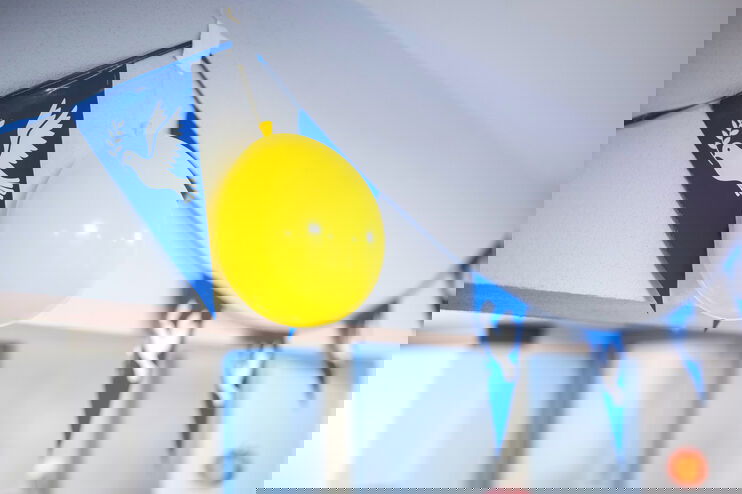Eine blaue Wimpelkette mit Friedenstauben, dazwischen hängt ein gelber Luftballon.