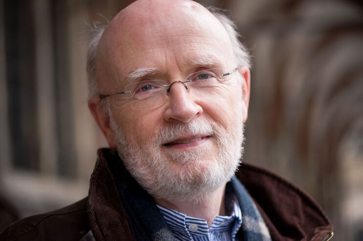 Eine als Mann lesbare Person mit hoher Stirn, grauem Bart und Brille