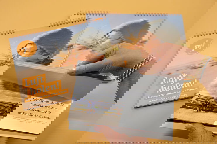 Auf einem orangenen Hintergrund liegen Kalender mit der Aufschrift "Luft holen". Jemand blättert durch einen hindurch.